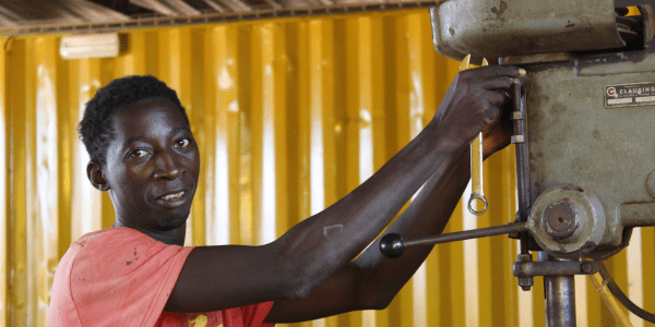 Welding graduate Augusto from Guinea-Bissau adjusts a drill press in a workshop.